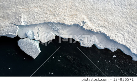 Melting iceberg with large sections calving into dark ocean water 124936571