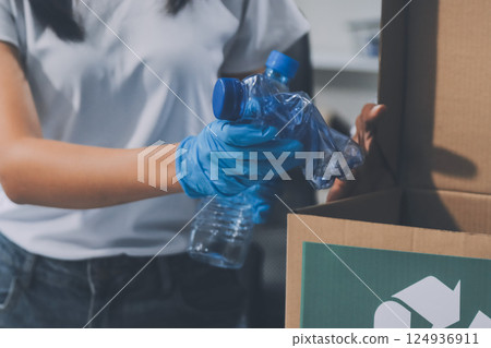 Close-up of female hands from a family collecting plastic waste and bottles from the ground. They wear gloves and focus on recycling to help reduce plastic pollution and protect the environment. 124936911
