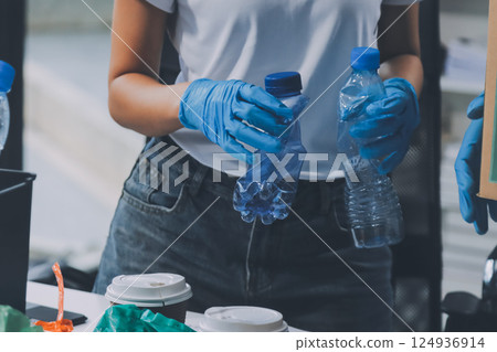 Close-up of female hands from a family collecting plastic waste and bottles from the ground. They wear gloves and focus on recycling to help reduce plastic pollution and protect the environment. 124936914