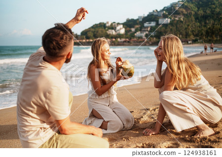 Friends Unwinding on the Beach with Refreshing Coconut Friends Unwinding on the Beach with Refreshing Coconut 124938161