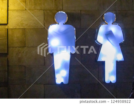 Neon illuminated public restroom sign with male and female figures on a dark wall 124938922