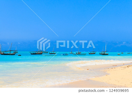 View of tropical sandy Nungwi beach and traditional wooden dhow boats in the Indian ocean on Zanzibar, Tanzania View of tropical sandy Nungwi beach and traditional wooden dhow boats in the Indian ocean on Zanzibar, Tanzania 124939695