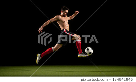 football player shows off his super fit body by using his right foot to balance a football in mid-air. 124941946