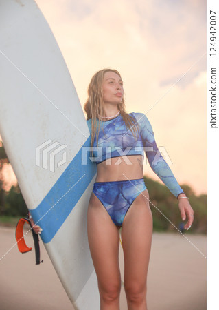 A woman wearing a bikini is standing on the beach while holding a surfboard A woman wearing a bikini is standing on the beach while holding a surfboard 124942007