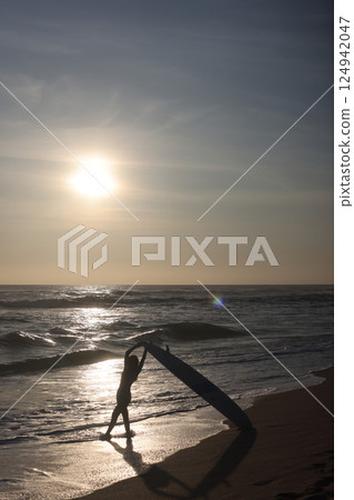 Silhouette of a Surfer Riding Waves at Sunset on the Beach, Full of Vibrant Colors 124942047