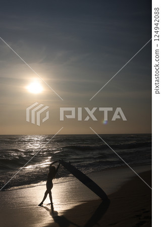 Silhouette of a Surfer Riding Waves at Sunset on the Beach, Full of Vibrant Colors 124942088