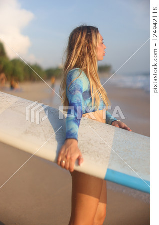 A young woman is enjoying an exhilarating surfing experience at sunset on a beautiful beach A young woman is enjoying an exhilarating surfing experience at sunset on a beautiful beach 124942118