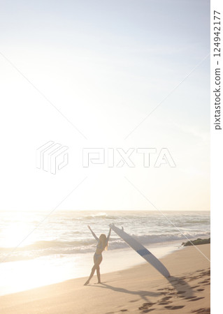 A person is standing on a sandy beach while holding a surfboard 124942177