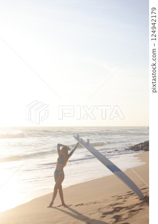 A person is standing on a sandy beach while holding a surfboard 124942179