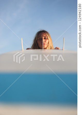 A woman is joyfully surfing at sunset with her surfboard against a clear blue sky A woman is joyfully surfing at sunset with her surfboard against a clear blue sky 124942180