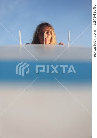 A woman is joyfully surfing at sunset with her surfboard against a clear blue sky 124942186