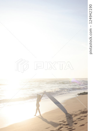 A person is standing on a sandy beach while holding a surfboard A person is standing on a sandy beach while holding a surfboard 124942190