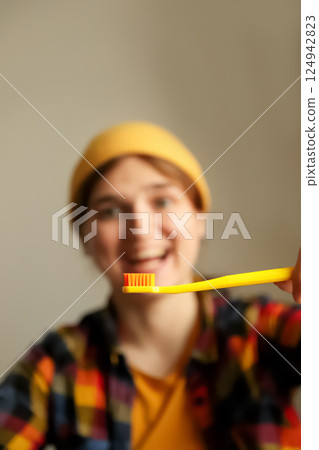 A woman with a playful, hipster style smiling while holding a yellow toothbrush, brushing her teeth in a fun and light-hearted way. The blurred background enhances the focus on her joyful expression 124942823