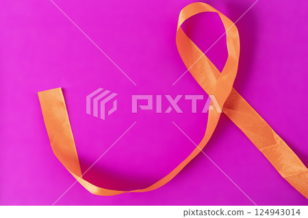 Orange ribbon on a vibrant pink background for awareness or decorative themes. 124943014