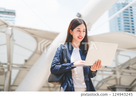 Business freelance adult asian woman using laptop standing on day building background 124943245