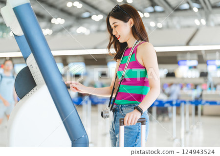 Woman passenger with travel luggage Using self service check in KIOSK at airport terminal Woman passenger with travel luggage Using self service check in KIOSK at airport terminal 124943524