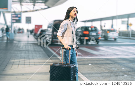 Standing tourist woman with travel luggage waiting at bus terminal for transport on day 124943536