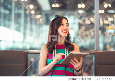 Tourist woman using digital tablet at international airport terminal for airline transport Tourist woman using digital tablet at international airport terminal for airline transport 124943539