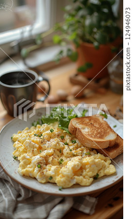 In a warm and inviting kitchen setting, a classic white plate holds perfectly cooked scrambled eggs seasoned with salt and pepper. The kitchen is adorned with rustic decor, soft lighting 124946073