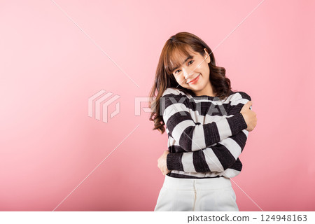 Happy beautiful young smiling Asian woman hugging herself remember a moment studio short isolated on pink background, Self care and self esteem concept, Lifestyle female love yourself carefree 124948163