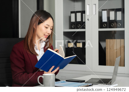 Female businessman use a laptopand take notes in the notebook at the office desk in the morning. Female businessman use a laptopand take notes in the notebook at the office desk in the morning. 124949672