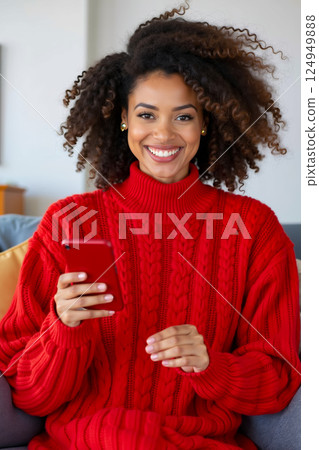 A woman in a red sweater sitting on a couch holding a cell phone 124949888