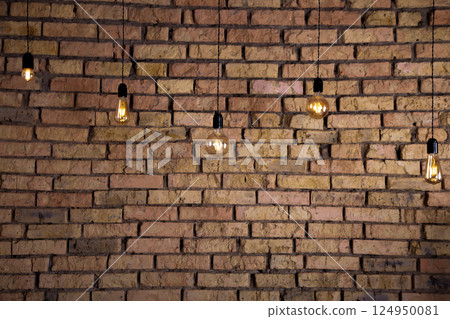 Old electric incandescent lamps with tungsten filament. Against the backdrop of a brick wall. Texture of old stone background. 124950081