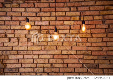 Old electric incandescent lamps with tungsten filament. Against the backdrop of a brick wall. Texture of old stone background. 124950084