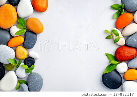 A border of colorful pebbles with green leaves on a white surface A border of colorful pebbles with green leaves on a white surface 124952117