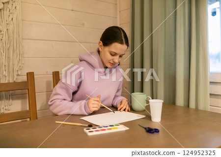 Young artist creating an artwork at a cozy table in a bright indoor space during the day Young artist creating an artwork at a cozy table in a bright indoor space during the day 124952325