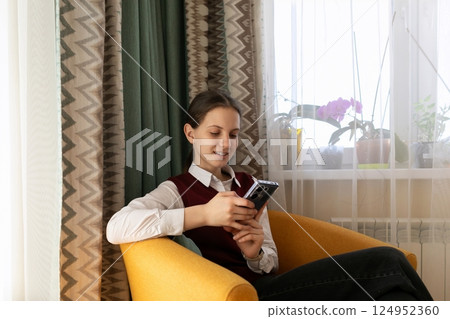 Young person using smartphone while sitting comfortably in bright room with plants and natural light Young person using smartphone while sitting comfortably in bright room with plants and natural light 124952360