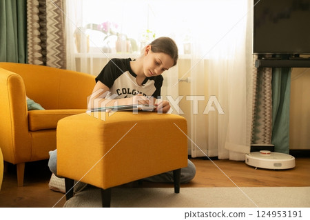 Young girl engaged in creative activity on a cozy yellow ottoman in a bright living room during 124953191