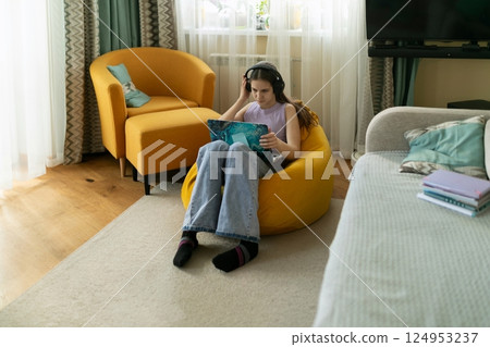 Young woman enjoys relaxing with a book while seated in a cozy bean bag chair in a bright living Young woman enjoys relaxing with a book while seated in a cozy bean bag chair in a bright living 124953237