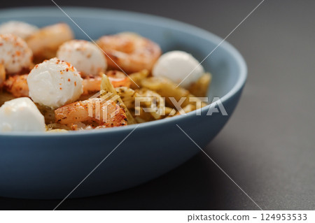 Penne pasta with shrimps and mozzarella and pesto in blue bowl with copy space 124953533