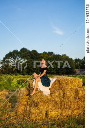 Young beautiful woman sits on a large pile of straw bales. Freedom, wind, setting sun. Young beautiful woman sits on a large pile of straw bales. Freedom, wind, setting sun. 124953786