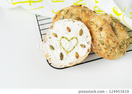 A delicious bagel with cream cheese and pumpkin seeds, featuring a heart-shaped design, sits on a cooling rack A delicious bagel with cream cheese and pumpkin seeds, featuring a heart-shaped design, sits on a cooling rack 124953819