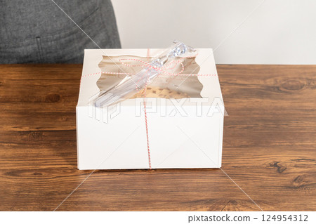 Carefully placing the gingerbread bundt cake, adorned with salted caramel frosting and gingerbread sprinkles, into a white paper bundt cake box with a clear window for gifting. 124954312