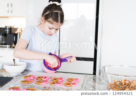 With focused attention, this budding culinary artist dips pretzels into a pot of melted chocolate, creating sweet delights in the warmth of a well-lit home kitchen. 124954321