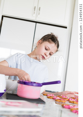 With focused attention, this budding culinary artist dips pretzels into a pot of melted chocolate, creating sweet delights in the warmth of a well-lit home kitchen. 124954331