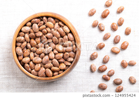 Pinto beans in a wooden bowl on linen fabric. Dried variety of common beans, Phaseolus vulgaris. Type of bean that are tan with reddish-brown specks. Most popular bean in Mexico and Southwestern USA. 124955424