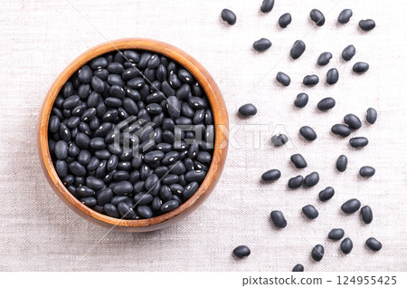 Black beans in a wooden bowl on linen. Dried variety of common beans, Phaseolus vulgaris, also known as black turtle beans, and caviar criollo. Type of bean with satiny black skin and a white center. Black beans in a wooden bowl on linen. Dried variety of common beans, Phaseolus vulgaris, also known as black turtle beans, and caviar criollo. Type of bean with satiny black skin and a white center. 124955425