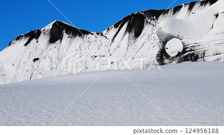 Black snowy mountains, snow fields and round holes against a blue sky 124956188