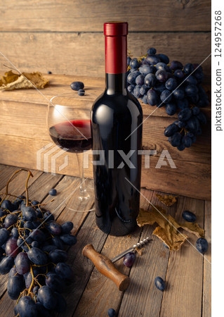 Bottle and glass of red wine with blue grapes on a wooden table. Bottle and glass of red wine with blue grapes on a wooden table. 124957268