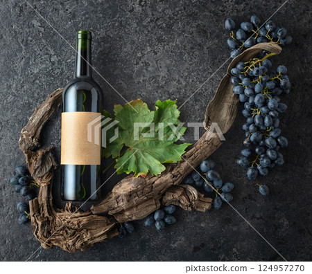 Bottle of red wine, blue grapes, and old vine snags on a black stone background. Bottle of red wine, blue grapes, and old vine snags on a black stone background. 124957270