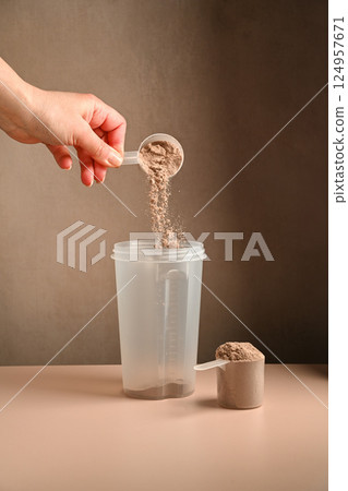 Making protein drink. Pouring chocolate protein powder in a shaker, food supplement concept 124957671