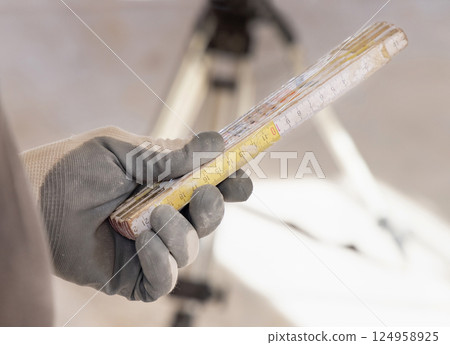 Craftsman in dusty glove holding a folded rule against horizontal rotary laser level 124958925