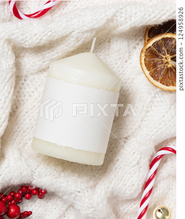 White pillar candle with blank label on white knitted sweater near Christmas decor, winter mockup White pillar candle with blank label on white knitted sweater near Christmas decor, winter mockup 124958926