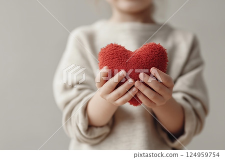A child holds a soft heart plush toy, symbolizing love and innocence. A child holds a soft heart plush toy, symbolizing love and innocence. 124959754