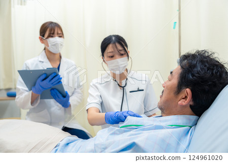 一名女護士在醫院病房檢查住院病人的生命徵象 一名女護士在醫院病房檢查住院病人的生命徵象 124961020