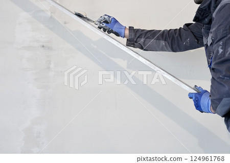 The hand holds a metal rule for leveling the plaster on the walls. Applying gypsum plaster in a mechanized way to the wall. High quality photo The hand holds a metal rule for leveling the plaster on the walls. Applying gypsum plaster in a mechanized way to the wall. High quality photo 124961768